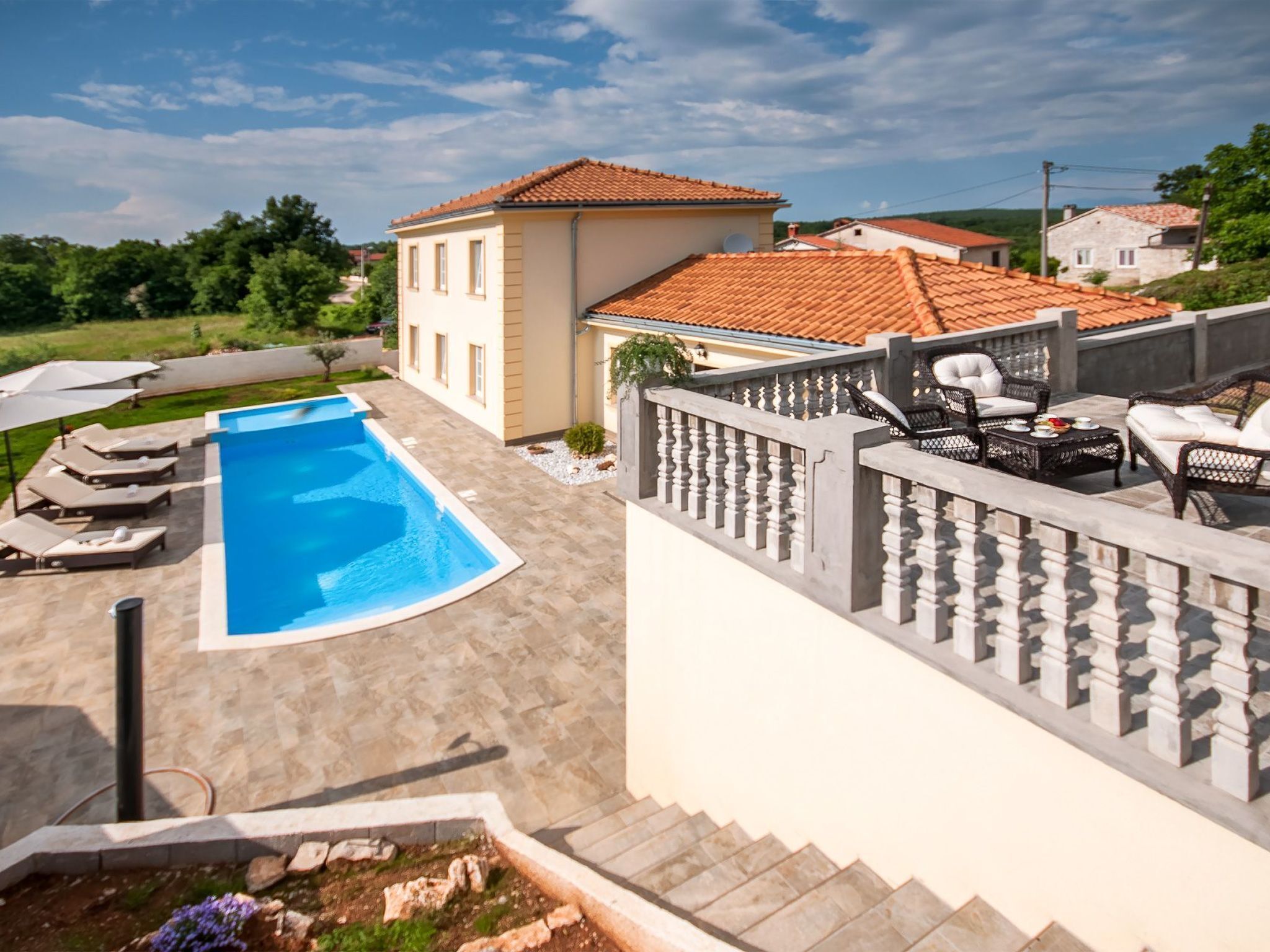 Une piscine avec des chaises longues, un patio couvert et une vue sur un bâtiment doté d’un toit en tuiles.