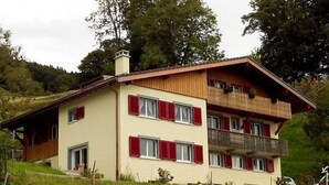 A two-story chalet with a sloped roof, red shutters, and a balcony on the upper floor. - Appartement dans une ferme rénovée by Interhome (Le Mont-Pèlerin)