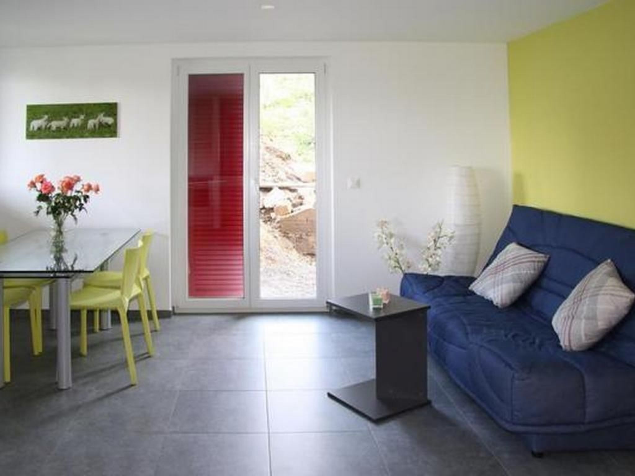 Una sala de estar moderna con un sofá azul, sillones amarillos, una mesa de vidrio y una puerta corredera roja.