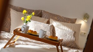 En säng med ett brickbord fullt av croissanter, en vas med gula blommor och två vita koppar.