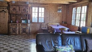 En stuga med träpanel på insidan, en svart lädersoffa, mönstrade golvplattor och en matplats med ett bord och stolar.