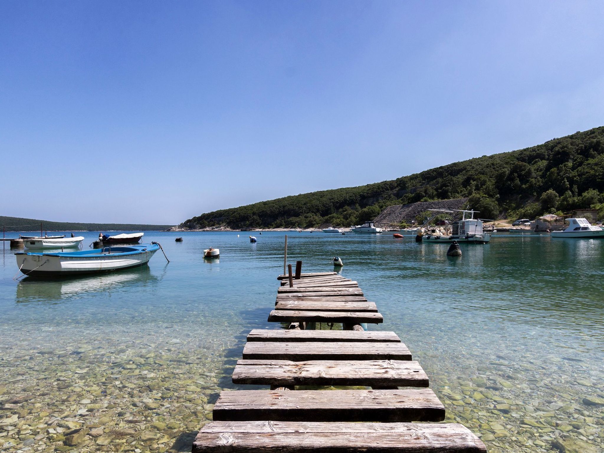 Une jetée en bois s’étendant dans une étendue d’eau calme, avec des bateaux amarrés à proximité.