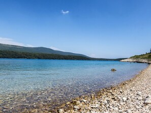 Ein klarer See mit steiniger Uferlinie und fernen Bergen.