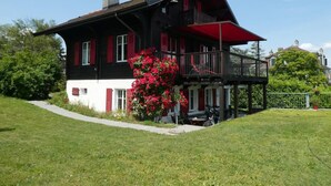 A two-story house with a balcony, a red flower bush, and a chimney. - Chalet am See in St-Prex by Interhome (Saint-Prex)