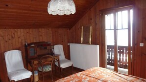 A wooden cabin bedroom with a bed, two chairs, a desk, and a radiator. - Chalet am See in St-Prex by Interhome (Saint-Prex)