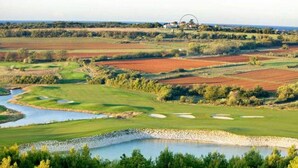 Een golfbaan met een vijver, zandbunkers en een gebouw in de verte.