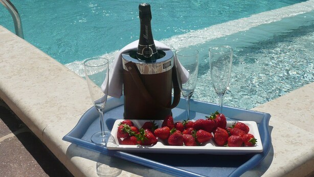 Een dienblad met een champagnefles, twee glazen en een schaal met aardbeien, bij een zwembad.