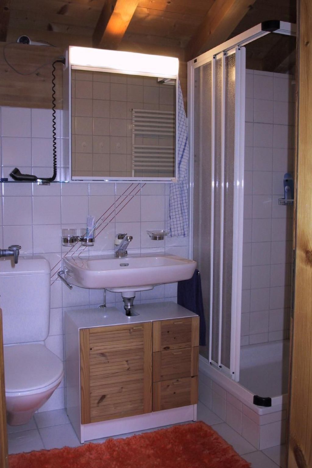 Une petite salle de bain avec un lavabo blanc, un meuble en bois et un espace douche.