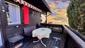 Een houten blokhut met een balkon, een tafel met een geruit tafelkleed en een rode deur.