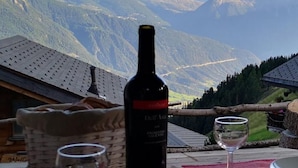 A table with a bottle of wine, a glass, and a plate of food with a mountain view in the background. - Chalt "Arve" by Interhome (Riederalp)