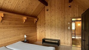 Une pièce en bois, avec un lit, un banc et une porte donnant sur une autre pièce.