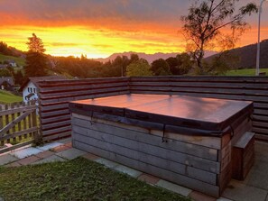 Ett bubbelbad med en trädeck och utsikt över en solnedgång över ett kuperat landskap.
