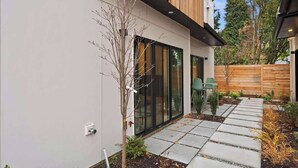A modern house with a large glass door, a small garden with a pathway, and a wooden fence in the background. - Modern Seattle Stay • Rooftop Views & Ensuite BRs (Seattle)