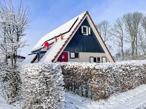 A snow-covered triangular house with a red door, surrounded by snow-laden bushes and trees. - Friesje by Interhome (Anjum)