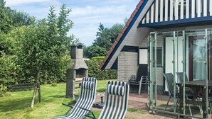 Talo, jossa on lasiseinillä varustettu patio, kaksi raidallista aurinkotuolia, tiilestä tehty savupiippu sekä puita ja nurmikkoa sisältävä puutarha.