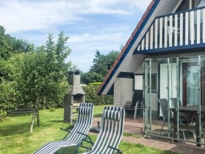 A house with a glass-enclosed patio, two striped lounge chairs, a brick chimney, and a garden with trees and grass. - Friesje by Interhome (Anjum)