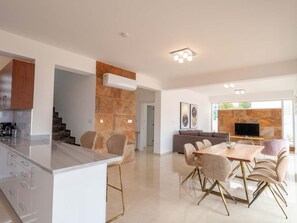 A modern kitchen with a marble island, a dining area with a glass-top table and gold-legged chairs, and a living area with a stone fireplace and a flat-screen TV. - Luxuriöse Villa mit 4 Schlafzimmern, privatem Pool und Whirlpool by Interhome (Peyia)