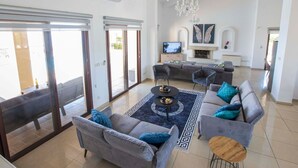 A spacious living room with a grey sofa set, a coffee table, and a chandelier. - Villa mit Blick auf die Berge und Whirlpool by Interhome (Kathikas Village)