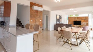 A modern kitchen with a marble island, a dining area with a glass-top table and gold-legged chairs, and a living area with a stone fireplace and a flat-screen TV. - Coral Elite Residence mit Pool und Whirlpool by Interhome (Peyia)