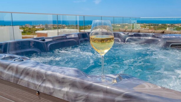 A hot tub with a glass of white wine, surrounded by a glass railing with a cityscape view. - Coral Elite Residence mit Pool und Whirlpool by Interhome (Peyia)