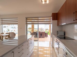 A modern kitchen with a large island, sliding glass doors leading to a patio area, and a view of a pool and outdoor seating. - Coral Elite Residence mit Pool und Whirlpool by Interhome (Peyia)