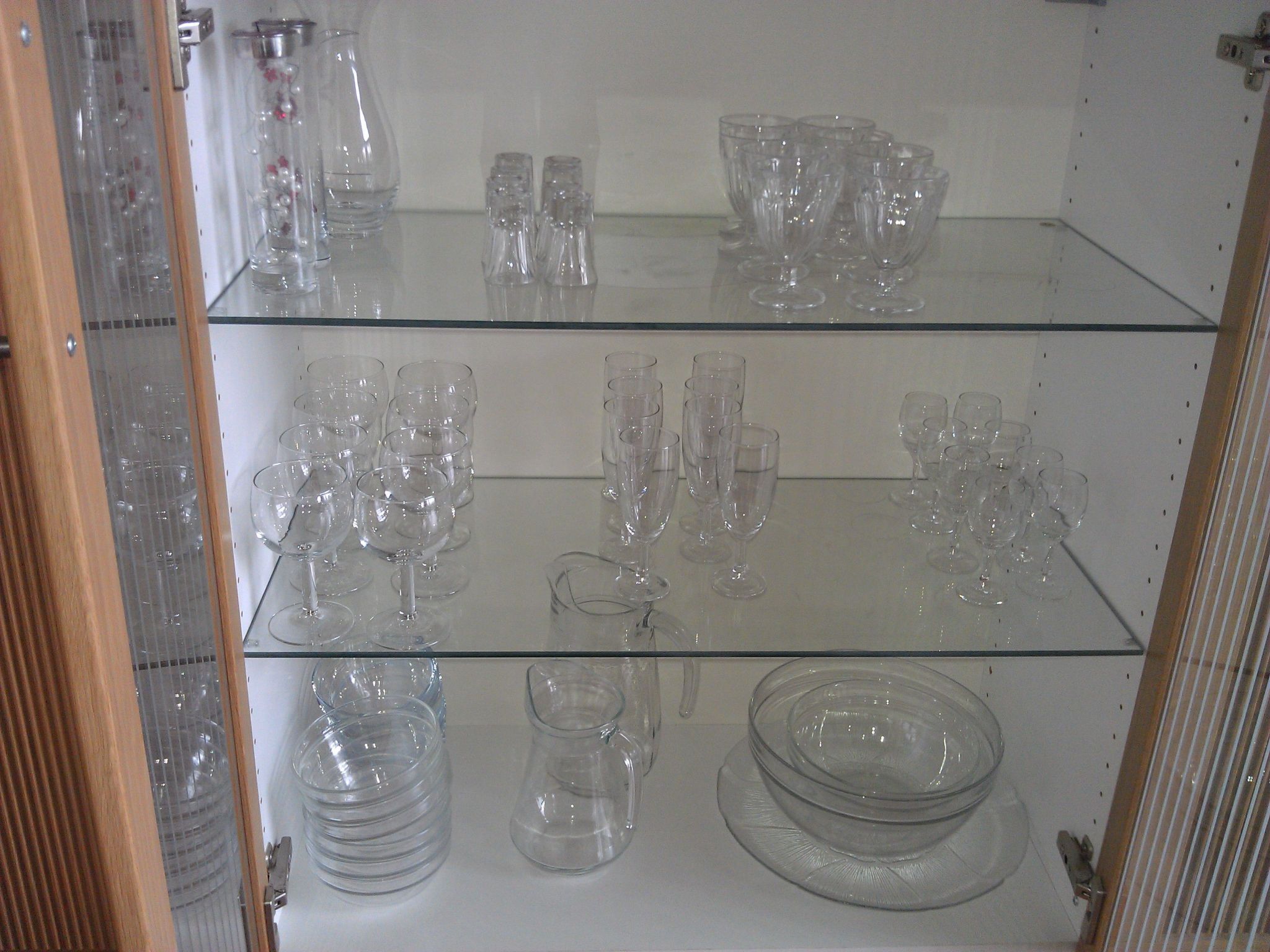 Een glazen vitrine met diverse glazen, waaronder wijnglazen, waterglazen en kommen.