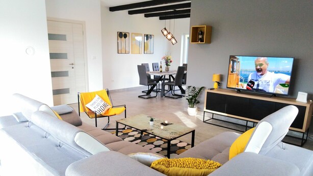 A modern living room with a grey sofa, yellow cushions, a coffee table, and a TV in the background. - mit Terrasse, Grill und Garten by Interhome (Umag/Juricani)
