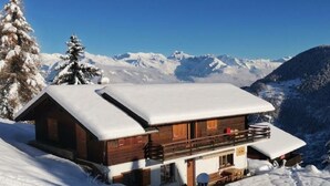 Une cabane en bois dotée d’un balcon, entourée de montagnes et d’arbres couverts de neige.
