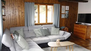 Un salon chaleureux avec un canapé d’angle, un meuble TV en bois et une petite table.