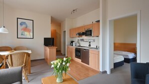 Una habitación de hotel compacta con comedor, kitchenette y cama.