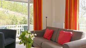 Una sala de estar con un sofá gris, cojines rojos, una mesa de centro de madera y un jarrón con flores blancas.