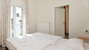 Una habitación de hotel con una cama, un ventanal con cortinas, un radiador y una puerta que da a otra habitación.