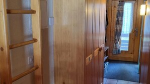 A narrow hallway with wooden walls and a tiled floor, leading to a door with a window. - Hüttbödeli by Interhome (Brienz)