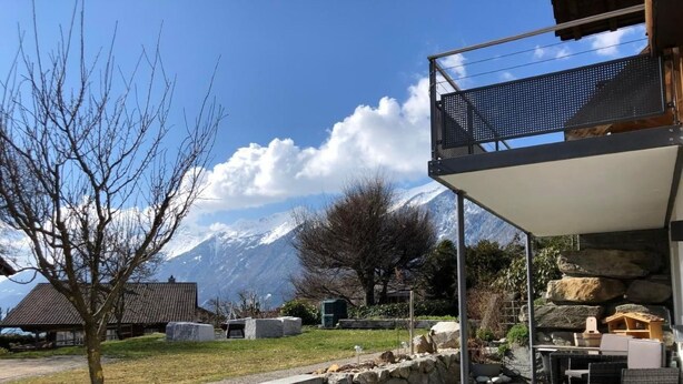 A modern outdoor seating area with stone steps leading up to a covered patio, overlooking a mountainous landscape.