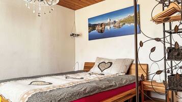 Une chambre à coucher avec un lit en bois, un lustre, un tableau représentant un paysage de montagne et un porte-vêtements fixé au mur.