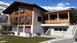 A modern two-story building with a wooden facade and large windows, set against a backdrop of snow-capped mountains.
