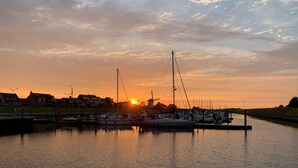 A marina at sunset with boats docked, calm water, and houses in the background.