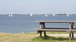 A wooden picnic table by a body of water with sailboats in the distance.