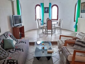 Un salon comprenant un canapé, une table basse, un téléviseur et un coin repas avec des chaises et une table.