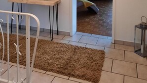 Una habitación con una cama, televisión, una mesita y un espejo. Hay una puerta que conduce a otra habitación.