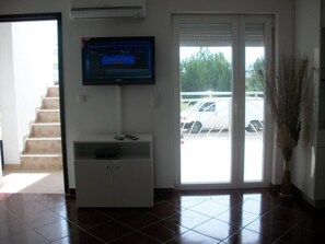 A reception area with a flat-screen TV mounted on the wall, a white console table with a remote control, and a large sliding glass door leading to a parking area. - Geräumige Ferienwohnung by Interhome (Vir)