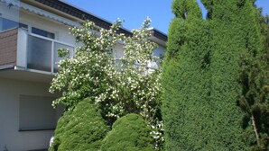 Een woongebouw met balkon, omgeven door verzorgde beplanting, waaronder een bloeiende boom en een hoge conifeer.