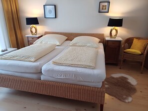 A double bed with white linens, two bedside tables with lamps, a wicker chair with a yellow cushion, and a framed picture on the wall. - Ambiente in Homberg ot Welferode by Interhome (Homberg (Efze))