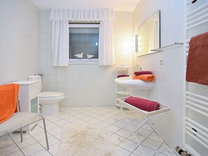 A bathroom with a toilet, sink, and window with curtains. There is a white rug on the floor and a towel rack with towels. - Ambiente in Homberg ot Welferode by Interhome (Homberg (Efze))