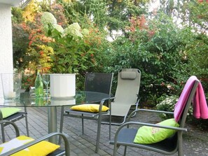An outdoor patio with metal chairs and a glass table, surrounded by lush greenery and flowering plants. - Ambiente in Homberg ot Welferode by Interhome (Homberg (Efze))