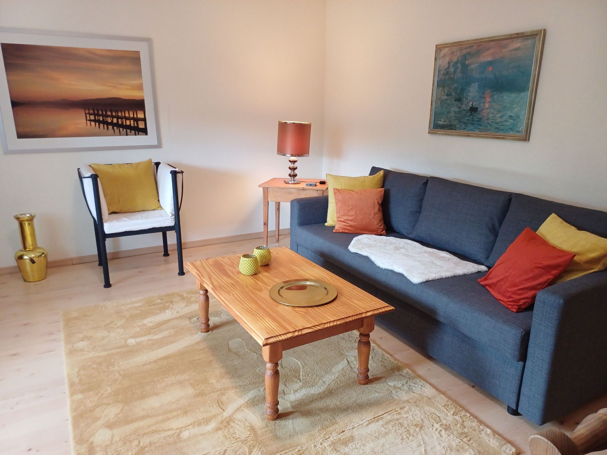 A living room with a sofa, a wooden coffee table, a chair, a lamp, and two paintings on the wall.