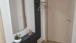 Een kamer met een donkerbruine console, een spiegel, een kleine potplant en een houten deur.
