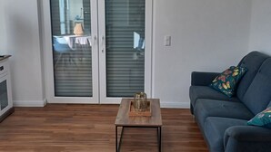 Een woonkamer met een donkerblauwe bank, een houten salontafel en een schuifdeur die leidt naar een balkon.