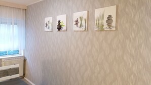 Ein Zimmer mit strukturierter Wand, einem Heizkörper und einem Fenster mit durchsichtigen Vorhängen.