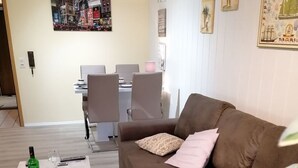 Ein Wohnzimmer mit braunem Sofa, einem weißen Couchtisch und einem Essbereich mit Stühlen und Tisch.